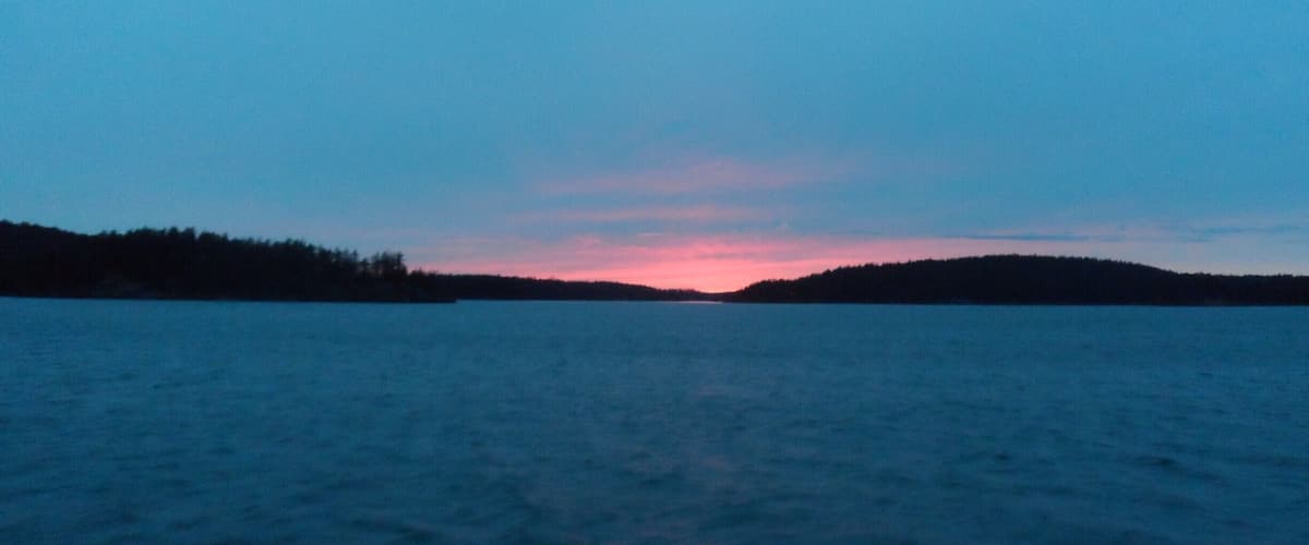 A calm lake at dusk with a pinkish sky and a forested shoreline.