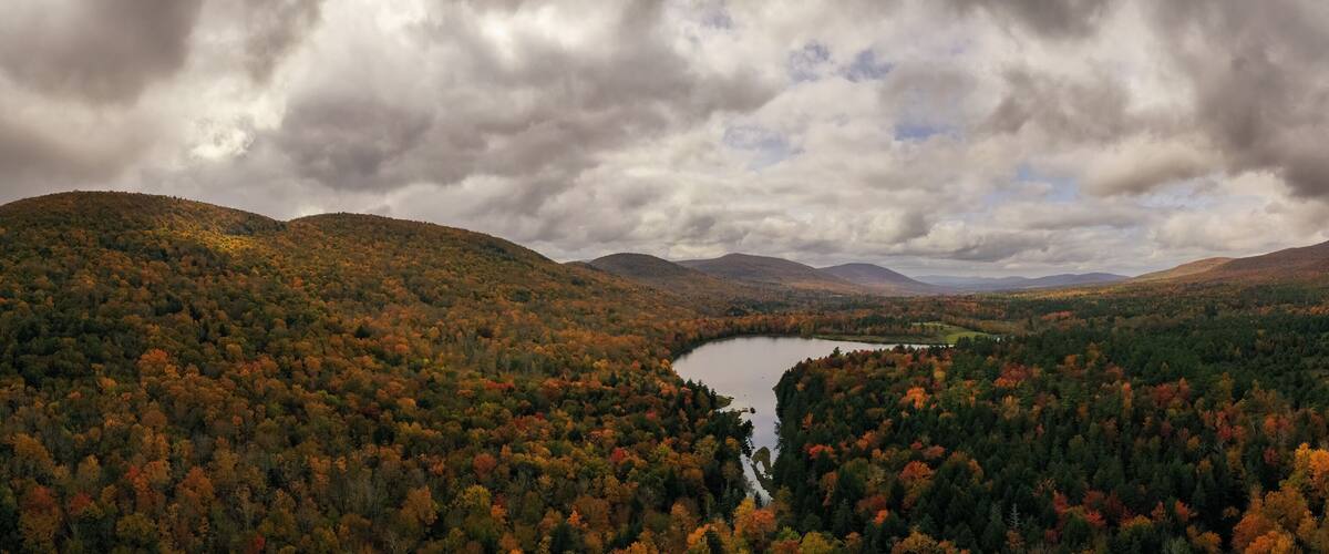 A lake surrounded by autumn-colored forest and mountains under a cloudy sky.