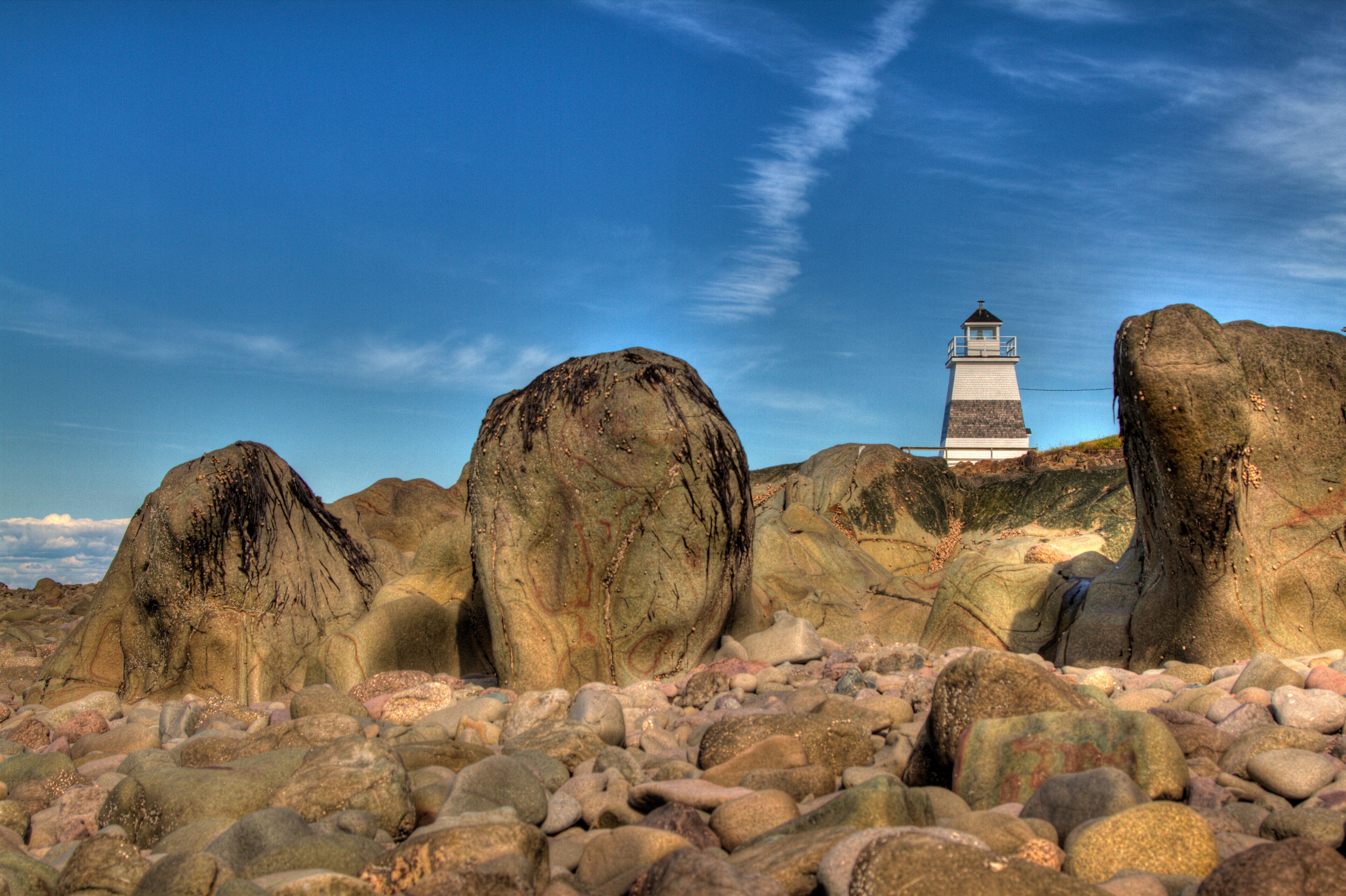 A lighthouse surrounded by large boulders on a rocky beach.