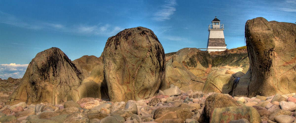 A lighthouse surrounded by large boulders on a rocky beach.