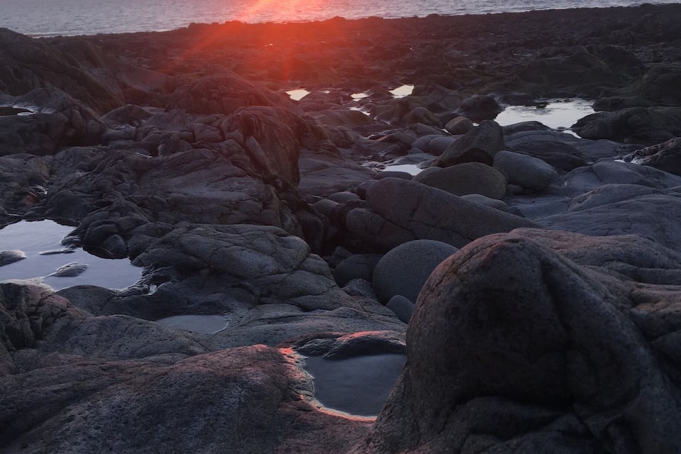 Una costa rocosa al atardecer, con el sol ocultándose en el horizonte.