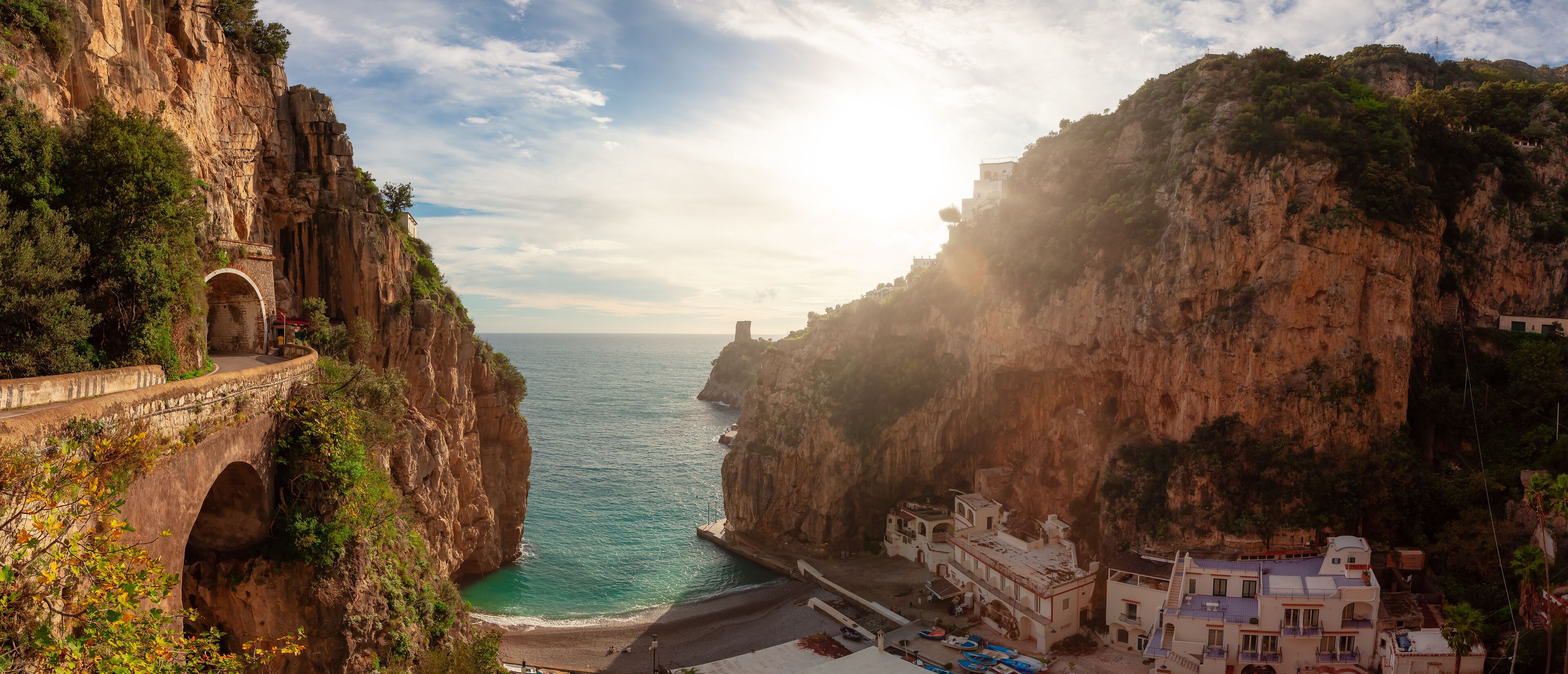 A coastal cliff with a stone bridge, a beach, and buildings on the cliffside.