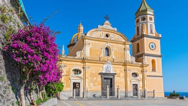 A yellow church with a bell tower and a dome, surrounded by a clear blue sky and a pink bougainvillea tree.