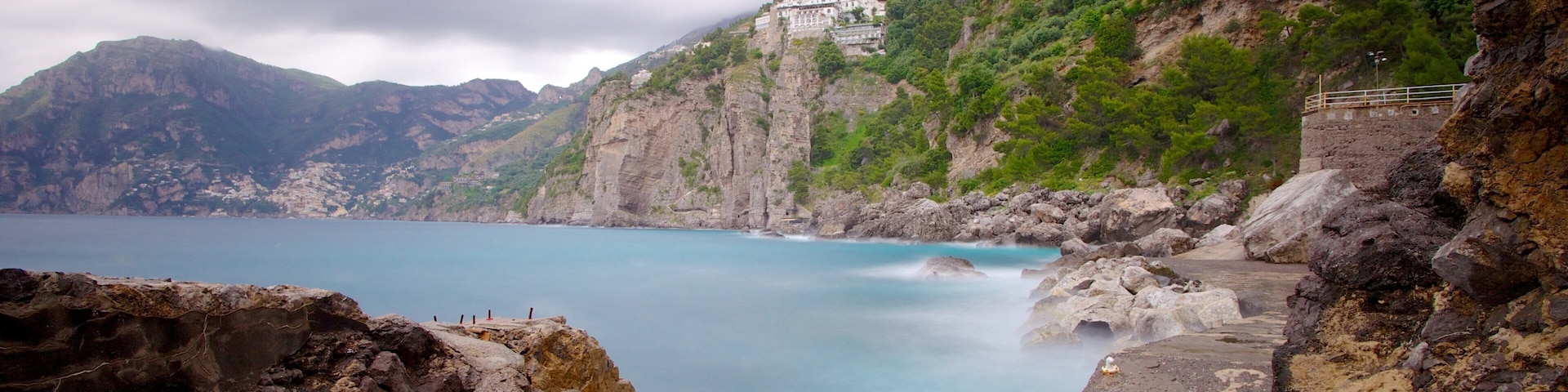 A coastal landscape with rocky cliffs, a clear blue sea, and a building on a hillside.