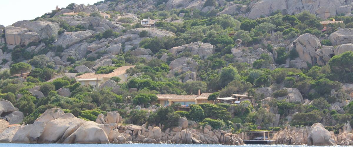 A coastal landscape with rocky hills, a sea in the foreground, and buildings on the hills.