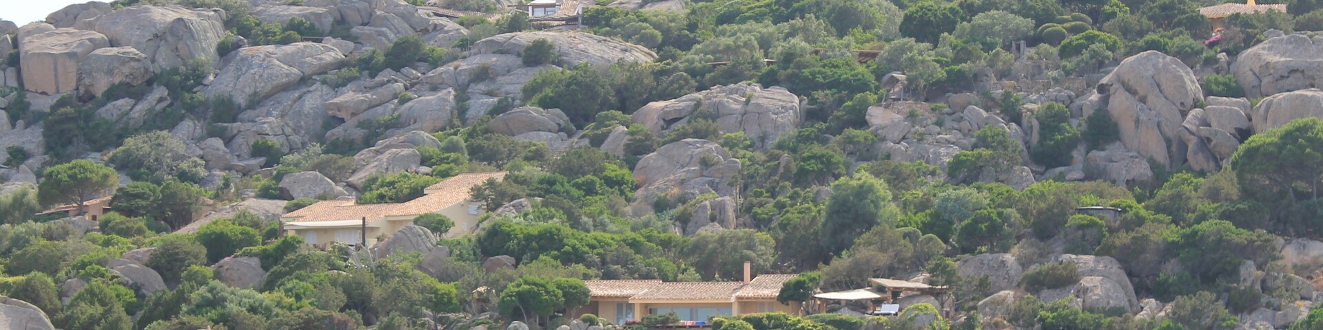 A coastal landscape with rocky hills, a sea in the foreground, and buildings on the hills.