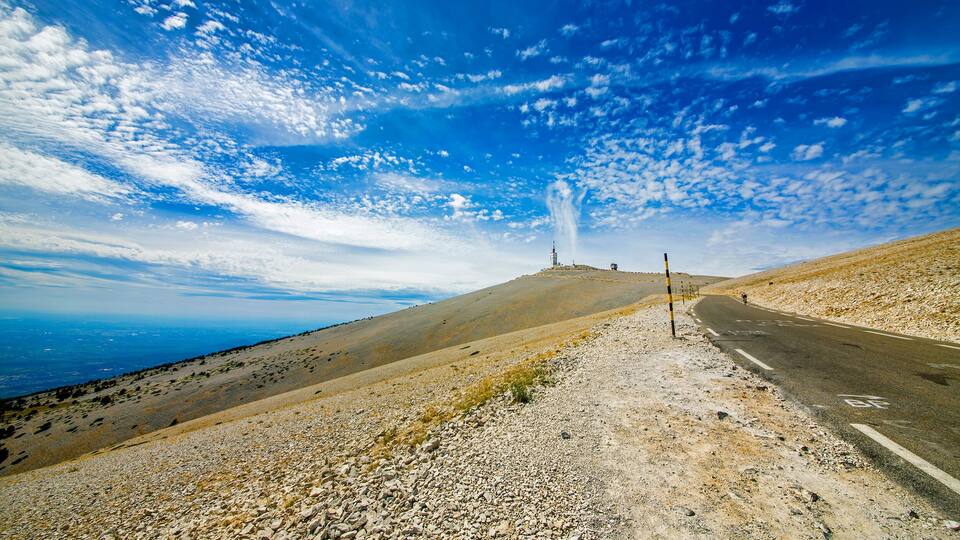 A road leading to a hilltop with a structure, under a partly cloudy sky.