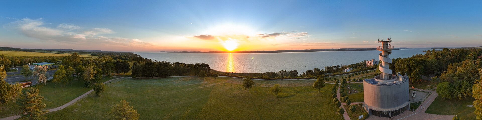 A sunset over a lake with a large industrial building and surrounding greenery.