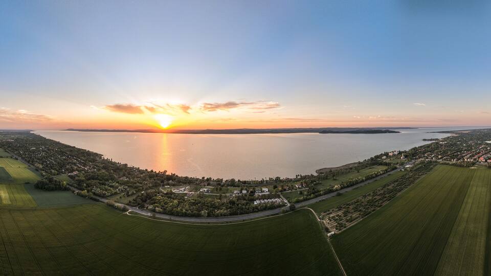 An aerial view of a coastal landscape with fields, a road, and a sunset over the water.