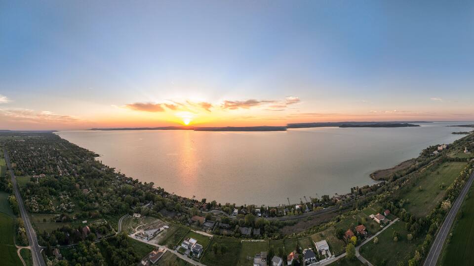 A sunset over a lake with surrounding residential areas and fields.