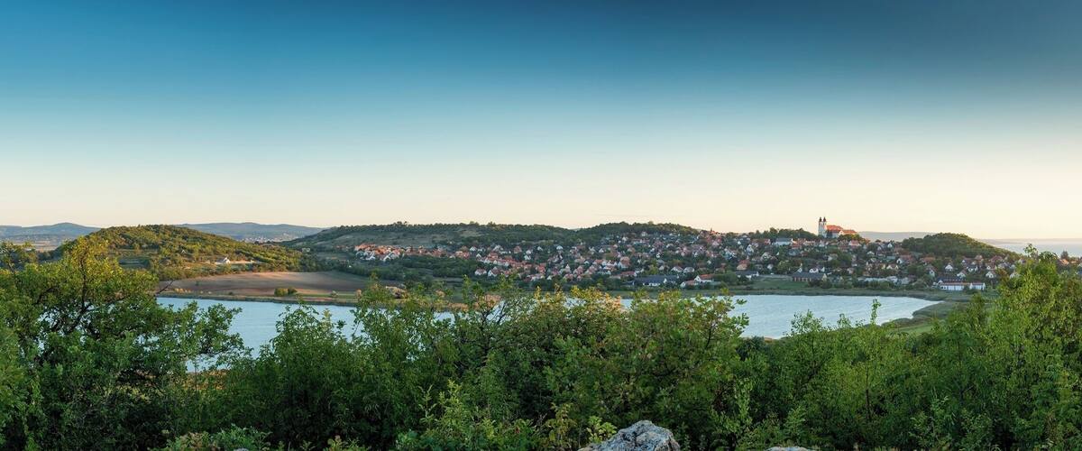 A coastal town with a prominent church on a hill, surrounded by greenery and a lake.