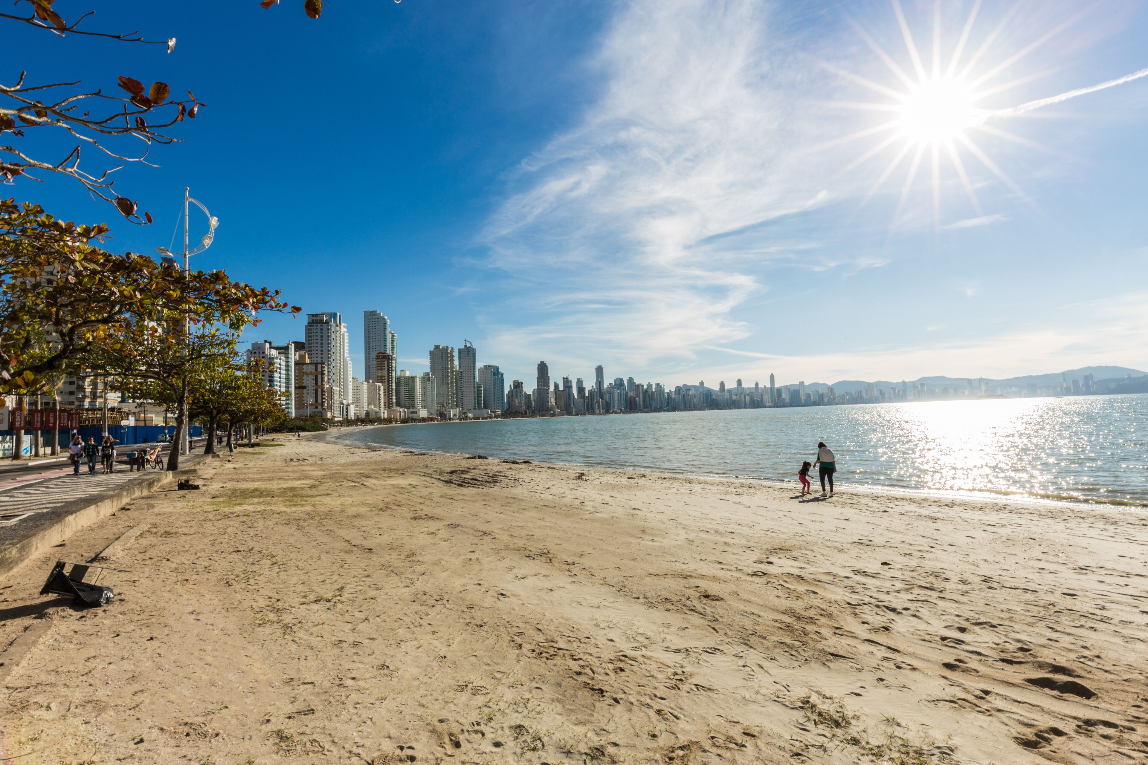 Uma praia arenosa com um horizonte urbano ao fundo e um céu azul límpido.