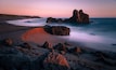 A rocky beach with a large rock formation at sunset.