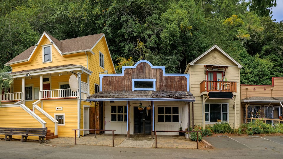 A yellow building with a porch and a wooden fence.