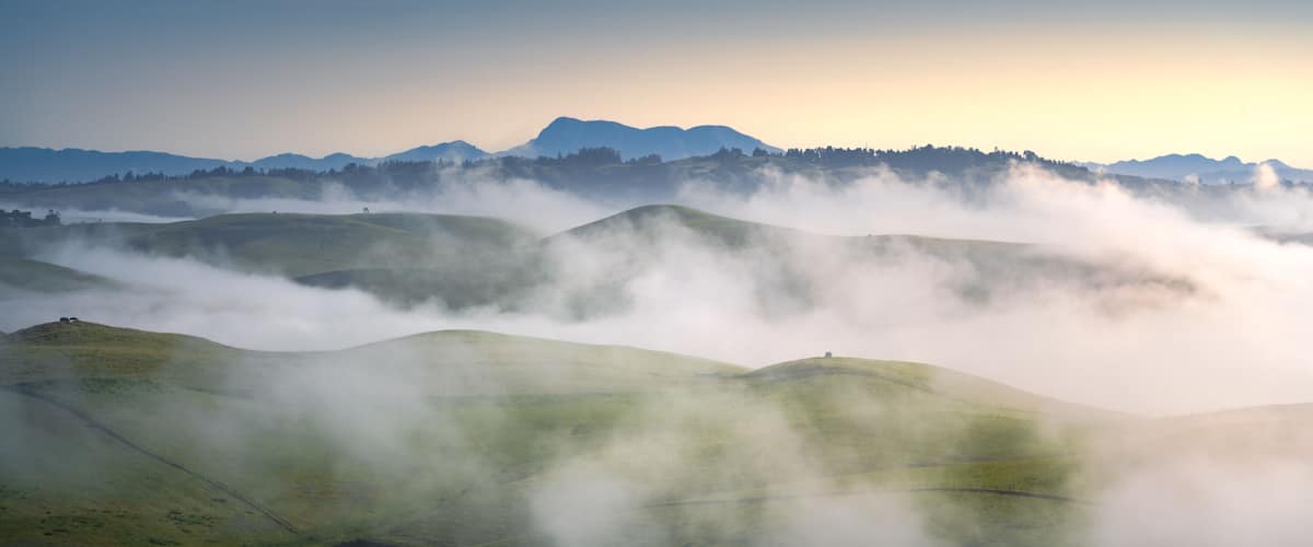 Rolling hills, a mountain range, and a valley shrouded in mist.