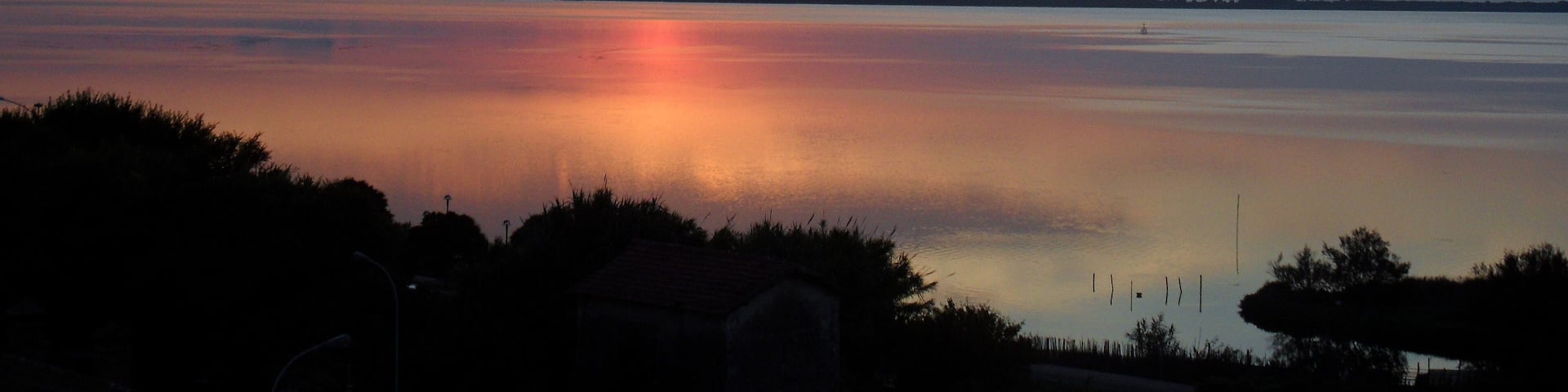 A sunset over a calm lake with silhouettes of trees and a distant shoreline.
