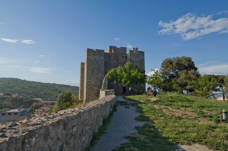 Un château de pierre auquel mène un sentier, entouré de verdure et de collines.