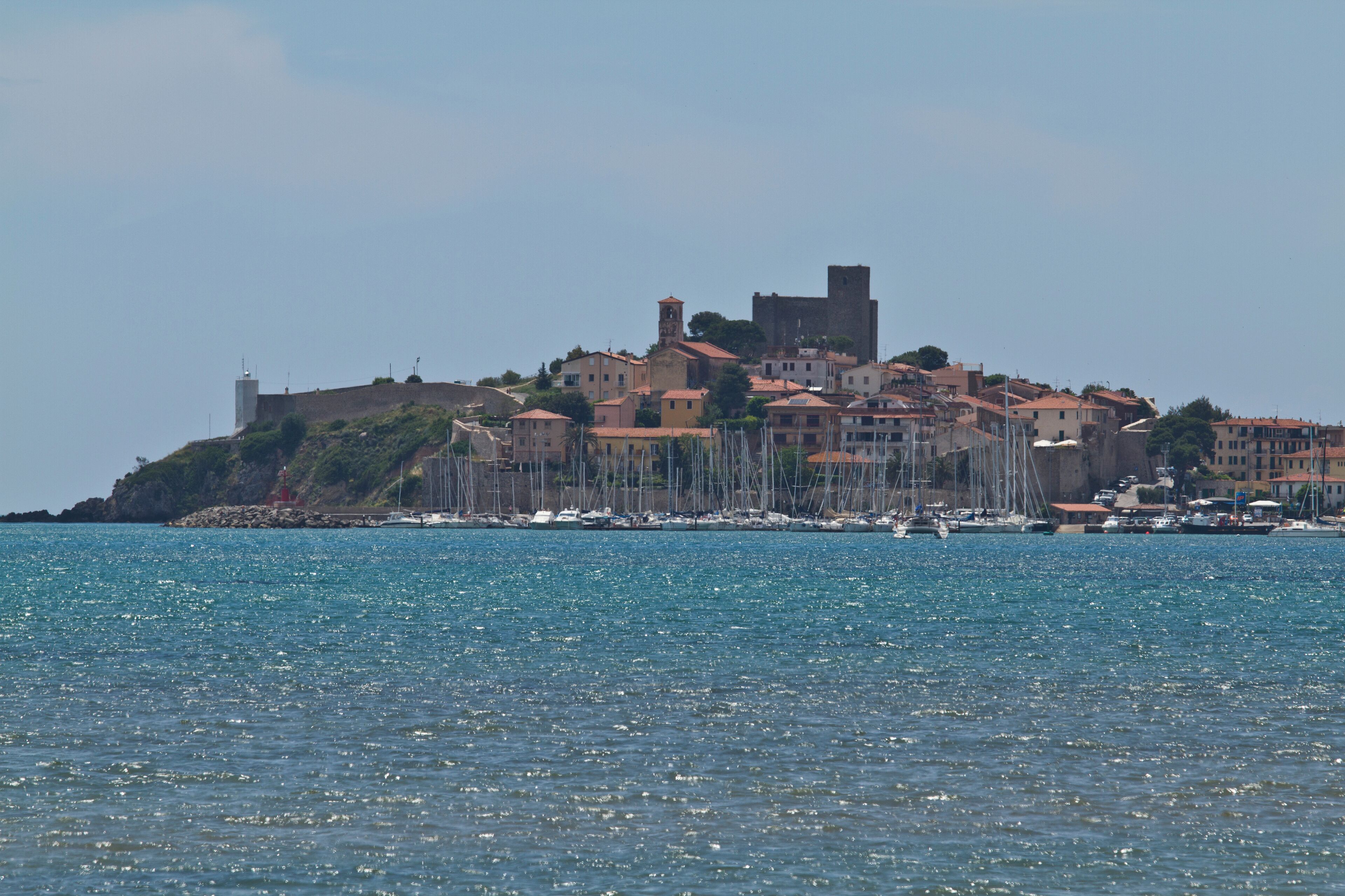 A coastal town with a prominent castle on a hill, surrounded by buildings and boats in the water.