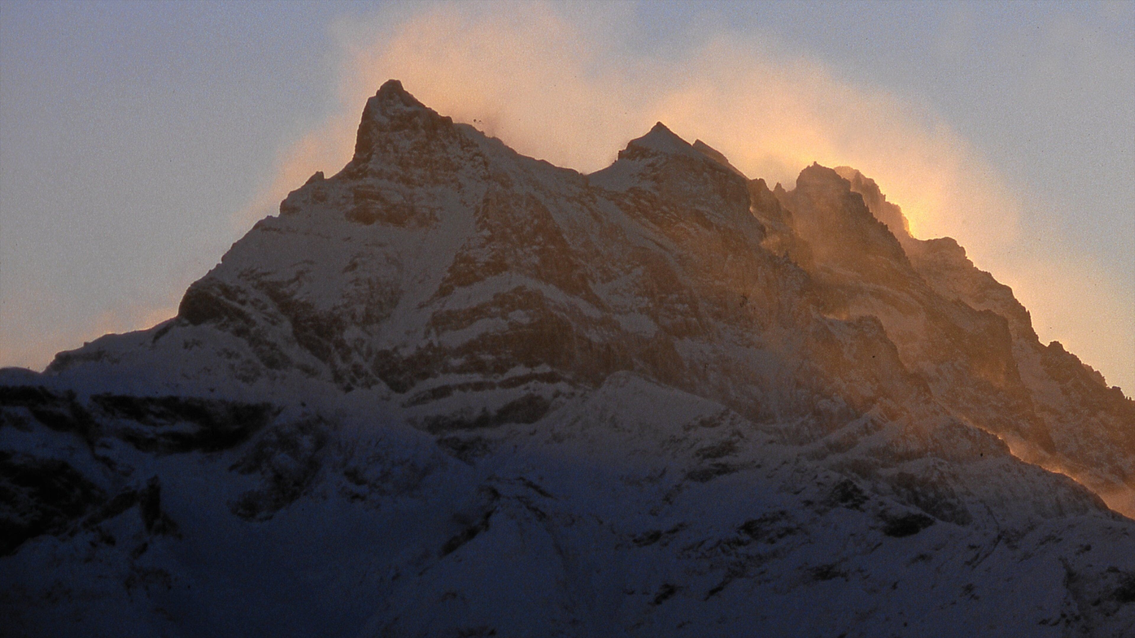 A snow-covered mountain peak with sharp ridges and a clear sky.
