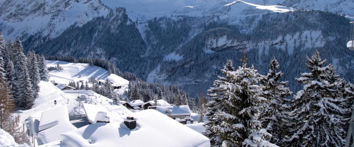 A snow-covered mountain landscape with peaks, trees, and buildings.