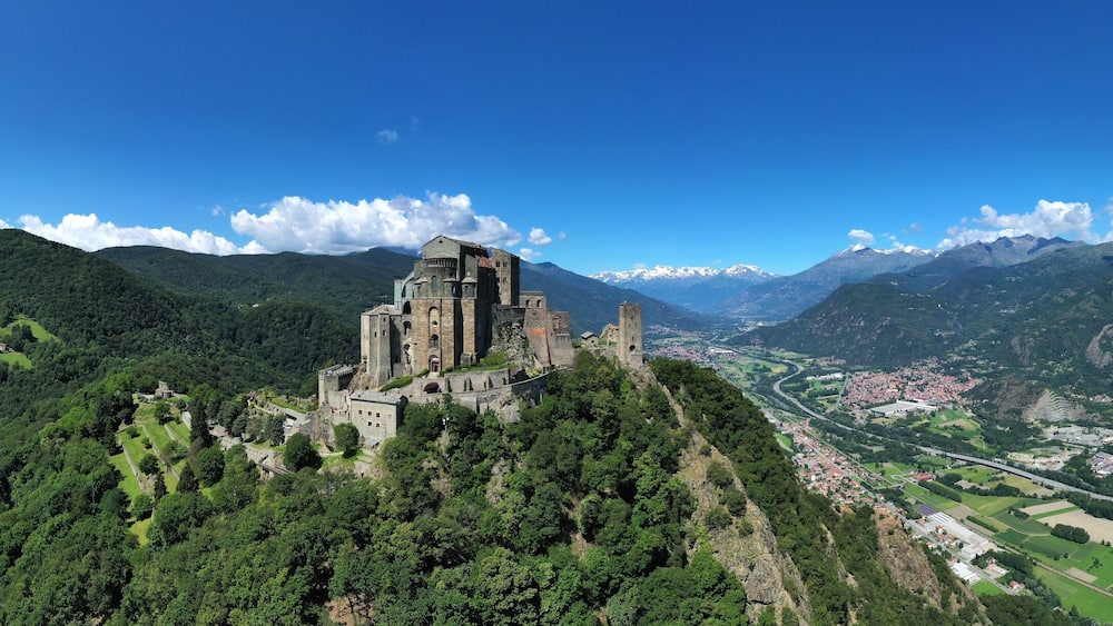 Eine Burg auf einem Hügel mit Blick auf ein Tal, einen Fluss und Berge im Hintergrund.
