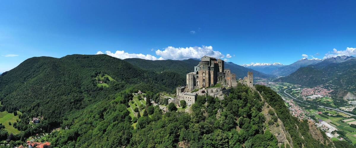 A castle on a hill overlooking a valley with a river and mountains in the background.