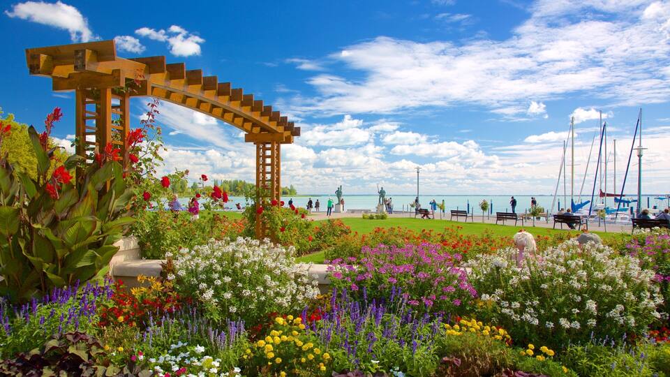 A garden with colorful flowers, a wooden pergola, and a view of the sea with boats.