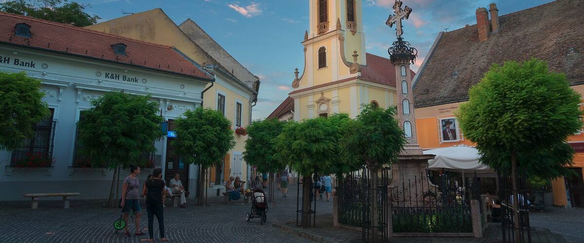 A cobblestone square with historic buildings, a church tower, and a statue.