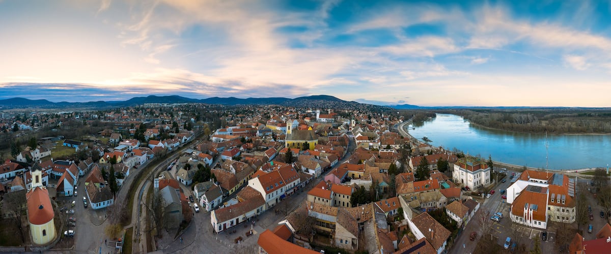Vista panorámica de un pueblo con un río, montañas al fondo e iglesia destacada.