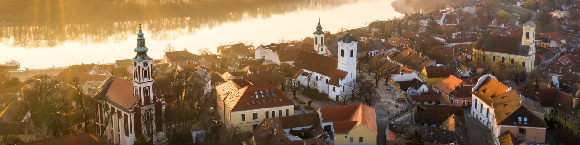 Un río que refleja el pueblo, una iglesia destacada y edificios residenciales circundantes.