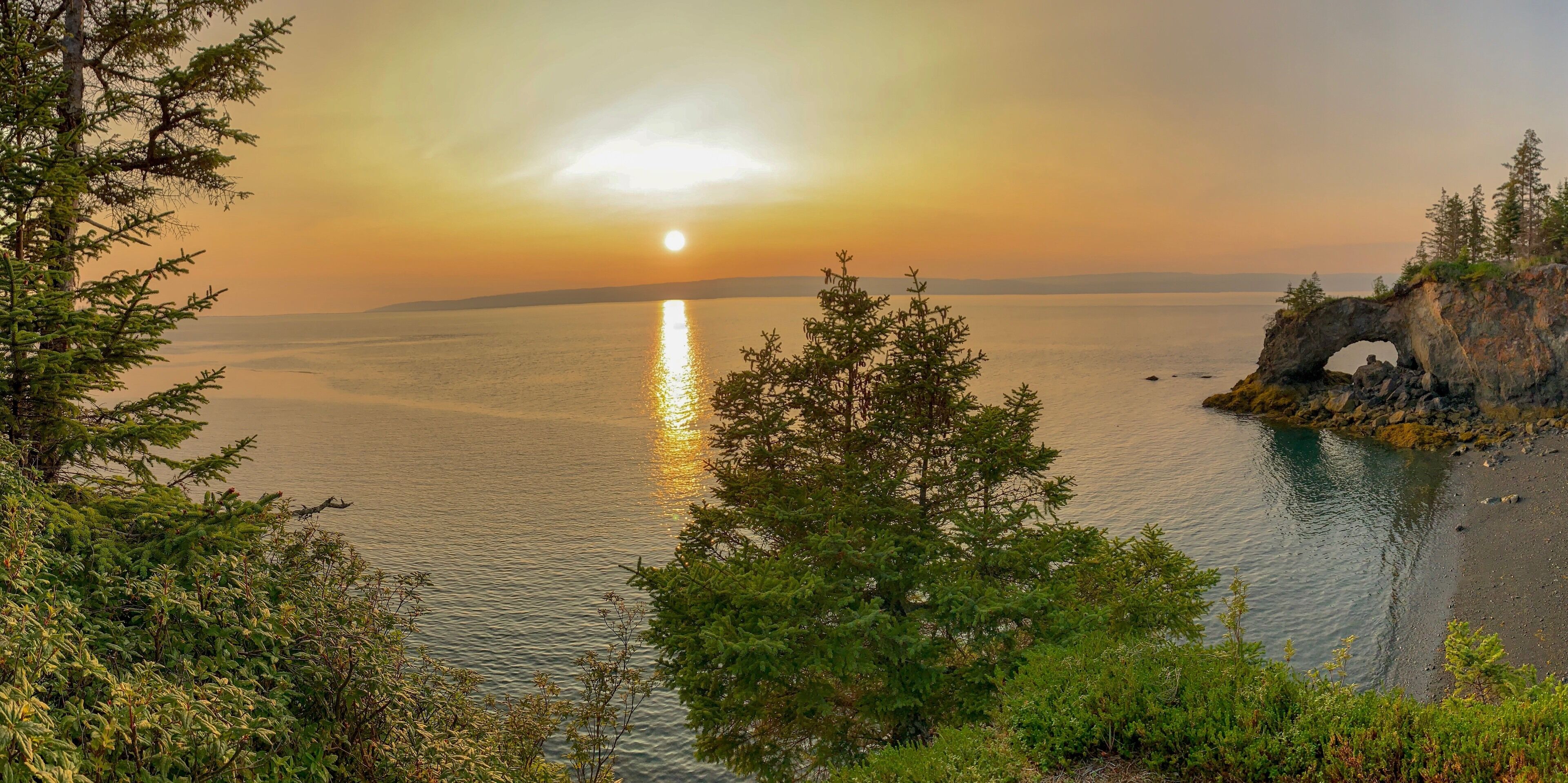A sunset over a calm sea with a rocky outcrop featuring a natural arch.