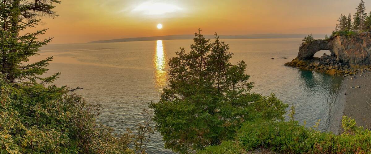 A sunset over a calm sea with a rocky outcrop featuring a natural arch.