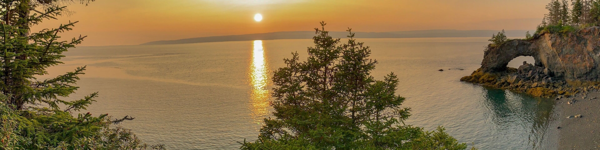 A sunset over a calm sea with a rocky outcrop featuring a natural arch.