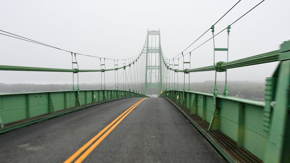 A green suspension bridge with a double yellow line in the center, spanning over a foggy landscape.