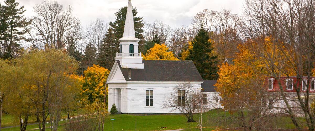 A white church with a steeple surrounded by autumn trees.