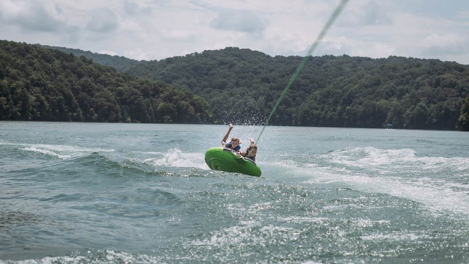 A person wakeboarding on a lake with a forested hill in the background.