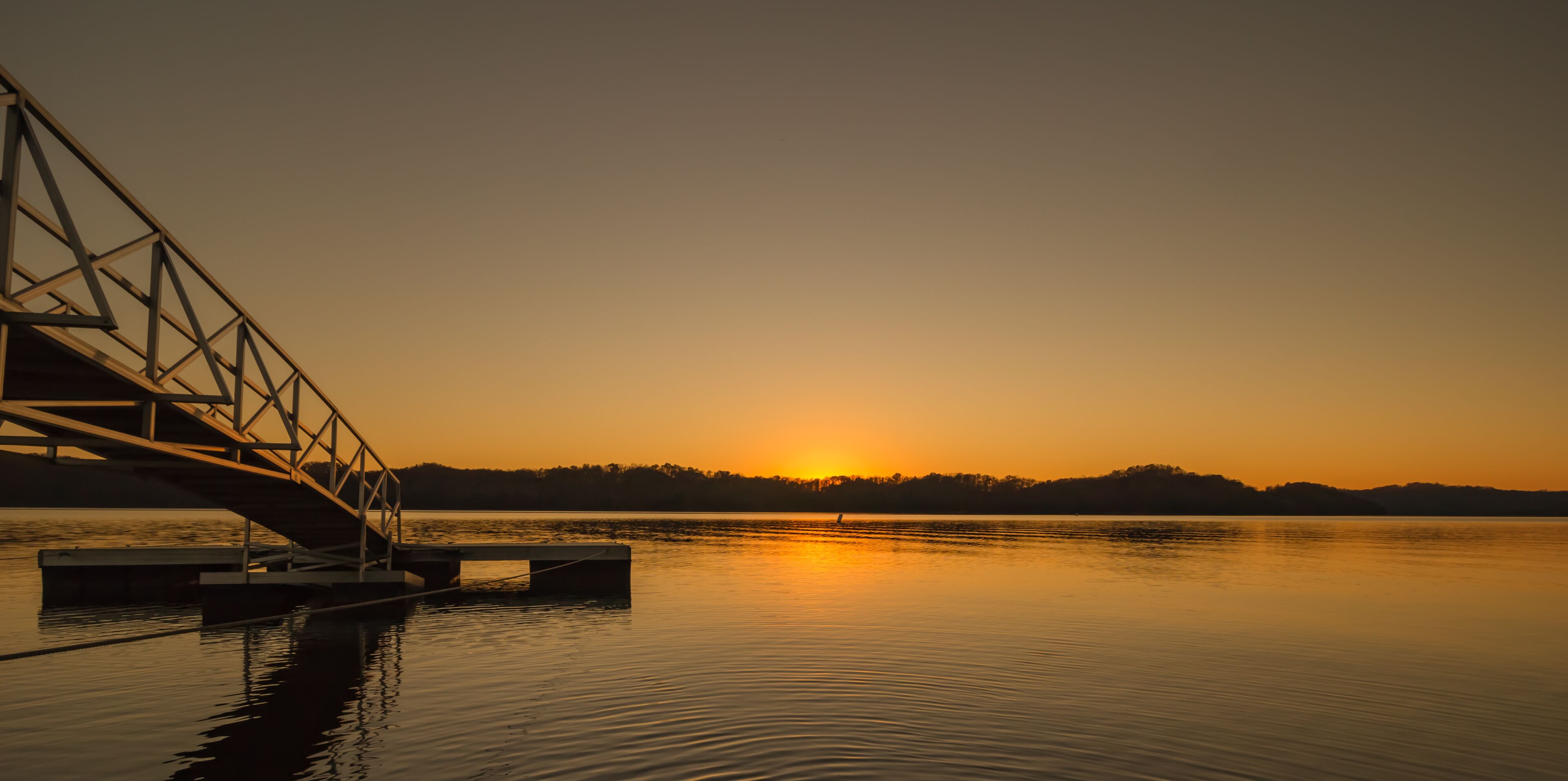 A sunset over a calm lake with a bridge in the foreground.