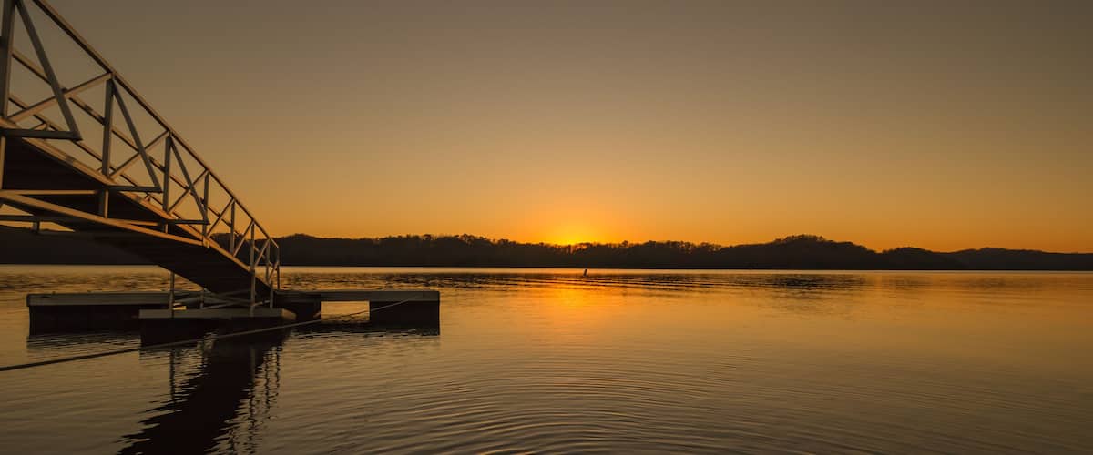 A sunset over a calm lake with a bridge in the foreground.