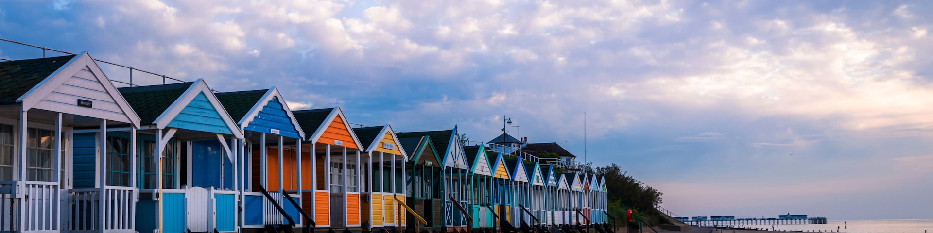 Uma fileira de cabanas coloridas à beira de uma praia arenosa, sob um céu nublado.