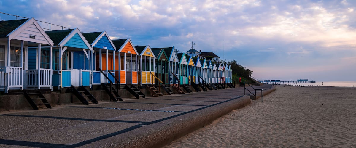 A row of colorful beach huts along a sandy beach with a cloudy sky.