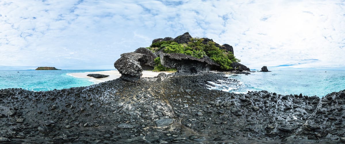 A rocky island with a small beach and turquoise waters.