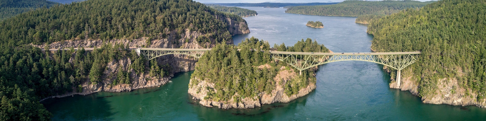 A bridge spanning a river with forested banks and mountains in the background.