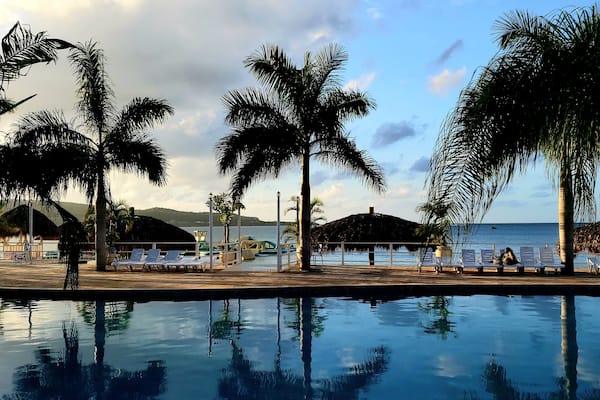 A poolside area with lounge chairs, palm trees, and a view of the ocean.