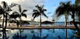 A poolside area with lounge chairs, palm trees, and a view of the ocean.