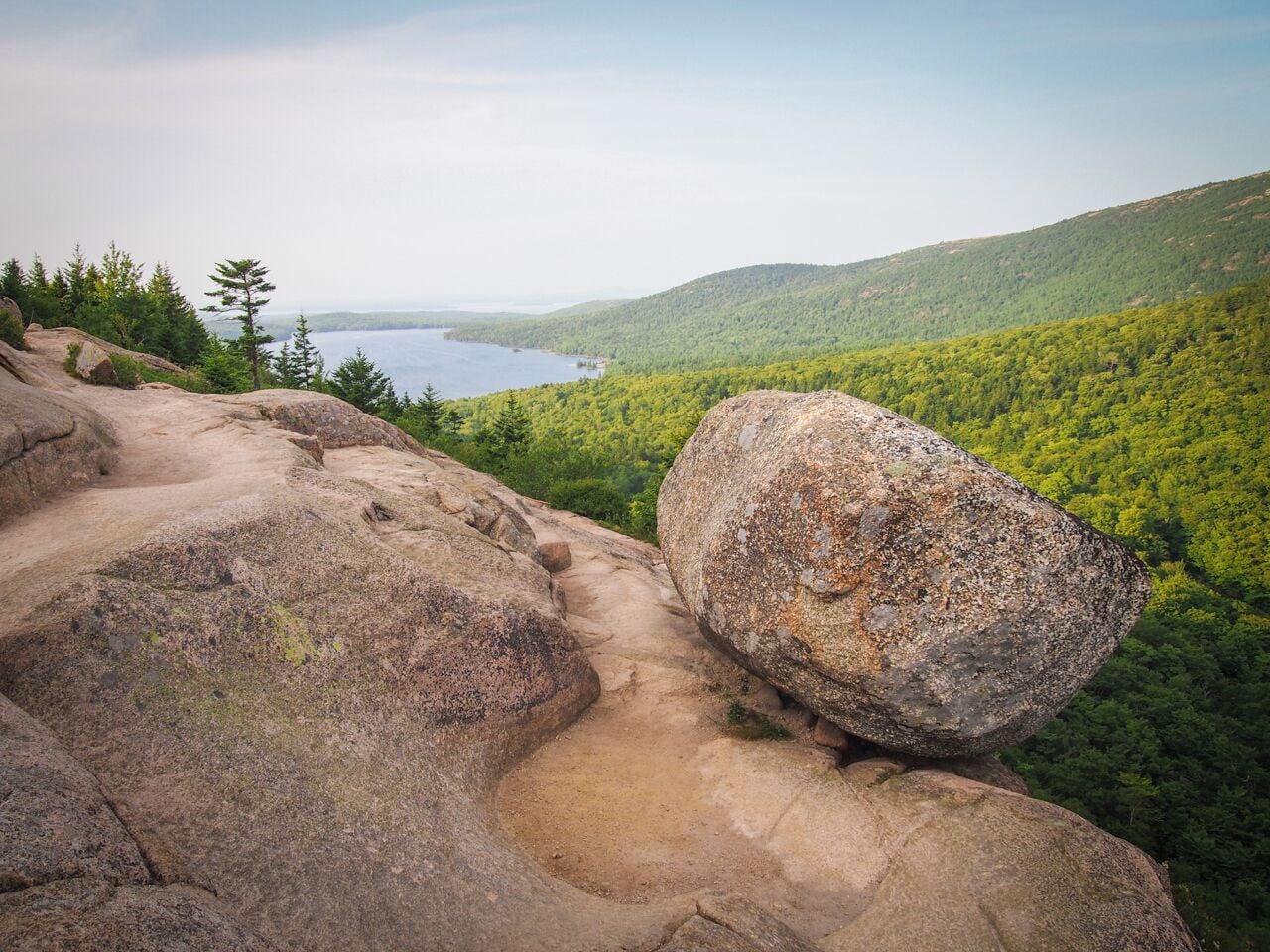 A rocky path leading to a lake surrounded by dense forest and hills.