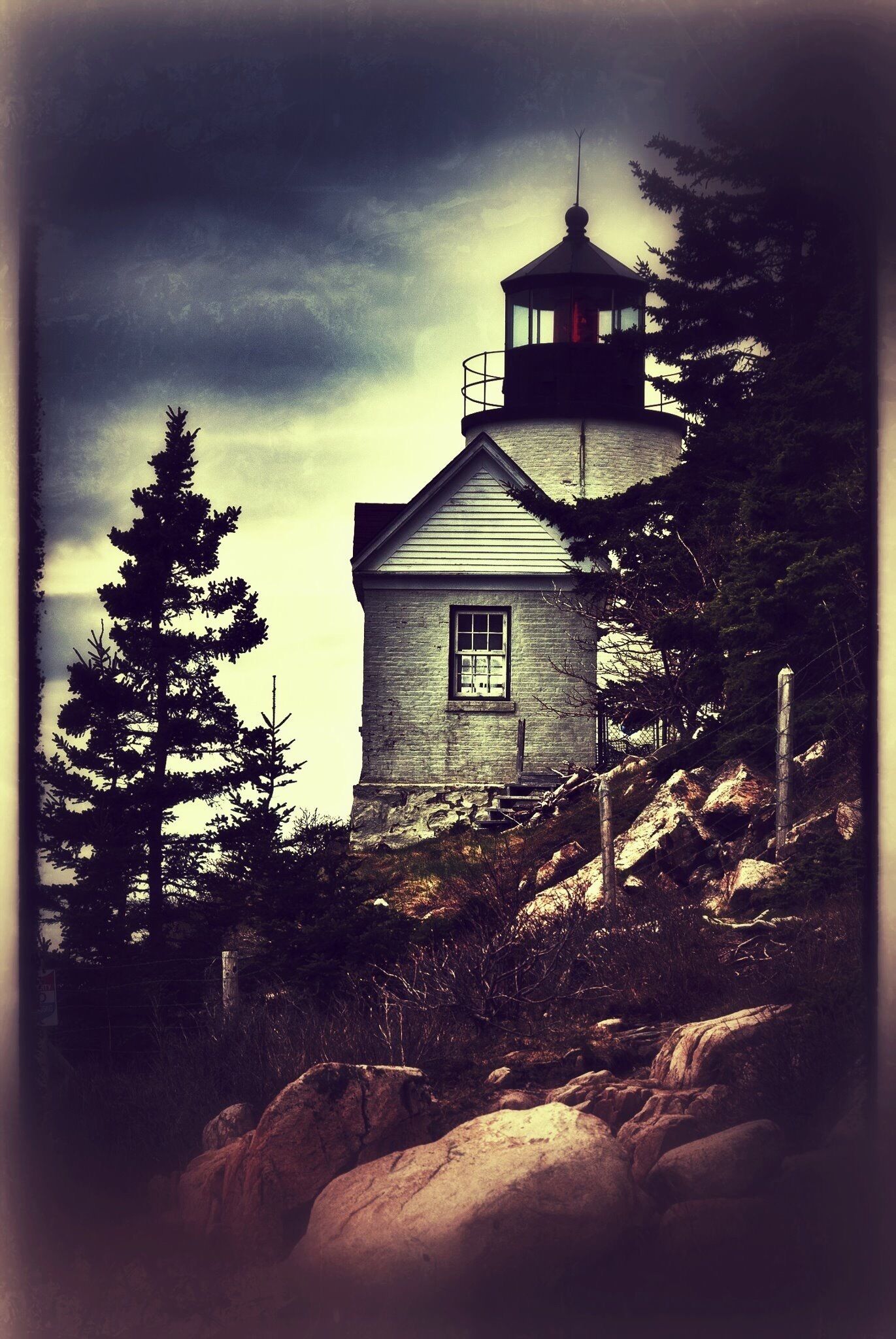 A lighthouse on a rocky hill with a forested background.