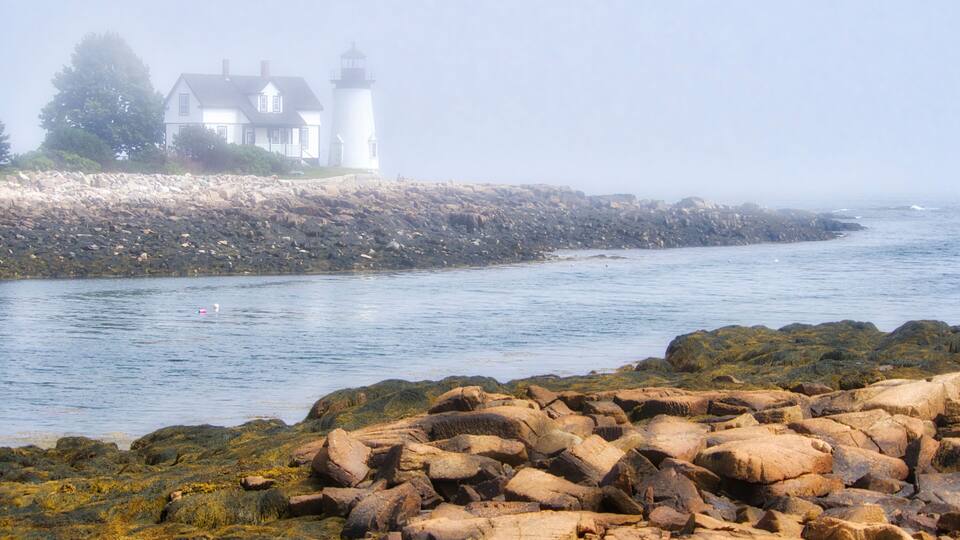 A rocky shoreline with a white house and lighthouse.