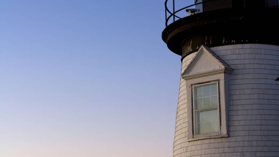 A lighthouse with a red light at the top, white brick walls, and a clear sky.