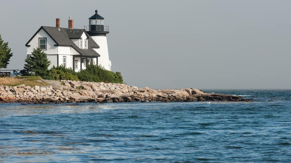 A white lighthouse with a black top, situated on a rocky shoreline by the sea.