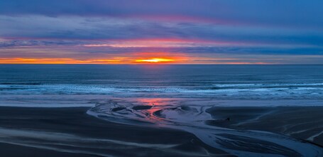 A sunset over a beach with calm waves and a clear sky.